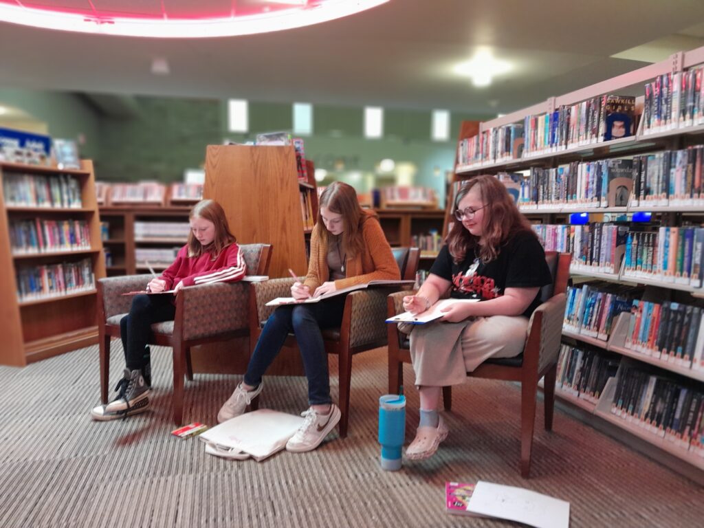 Three teenage girls sitting in chairs drawing