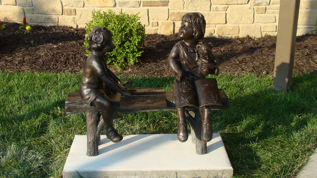 Statue of two kids reading a book on a bench in front of the Library building