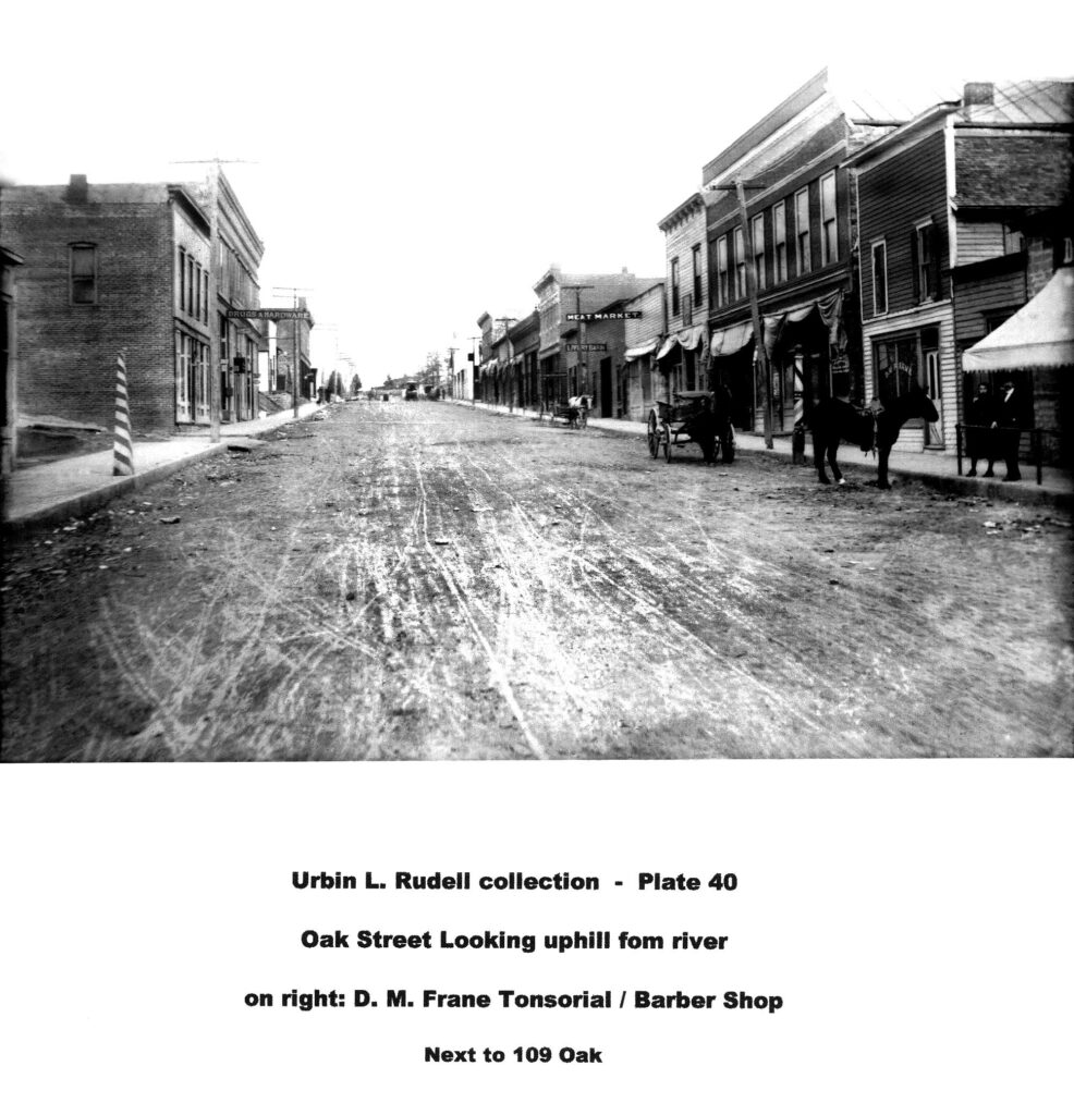 Urbin L Rudell collection plate 40. Oak Street looking uphill from river. On right: D M Frane Tonsorial/Barber Shop next to 109 Oak.